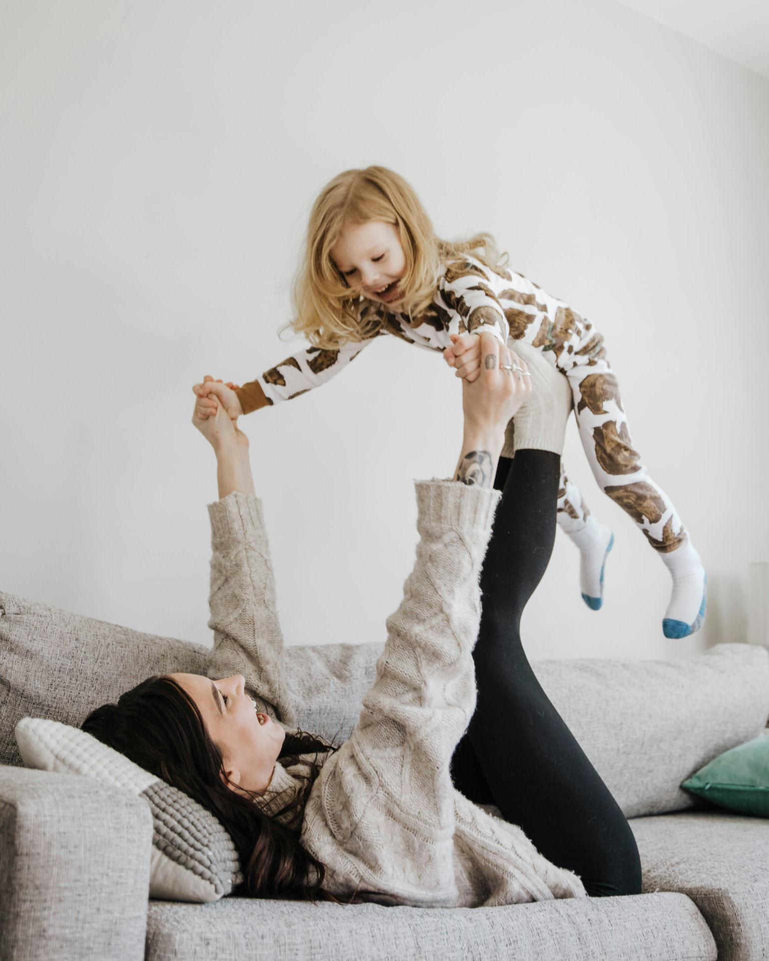 A parent on a sofa lifts a laughing child into the air during playful airplane play